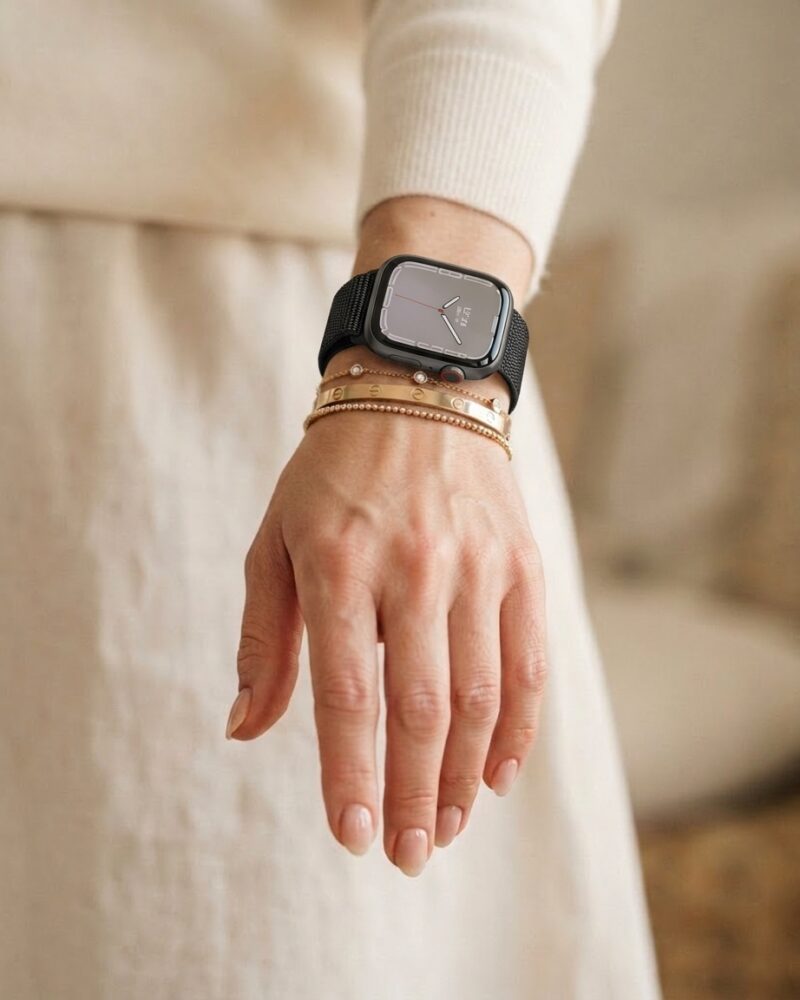 Black sport loop smartwatch on woman's wrist with layered gold bracelets