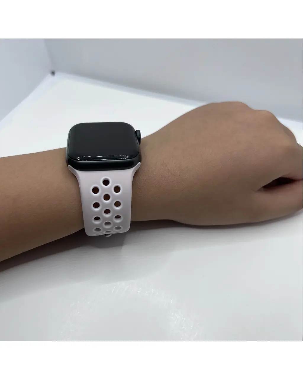 Black smartwatch with white perforated sport band on wrist